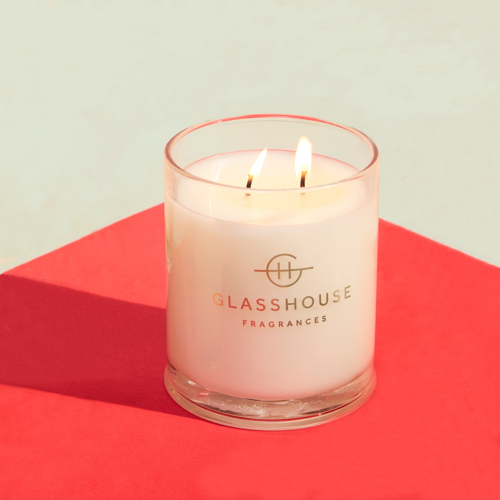 Glasshouse Frangrances soy candle burning on red tabletop