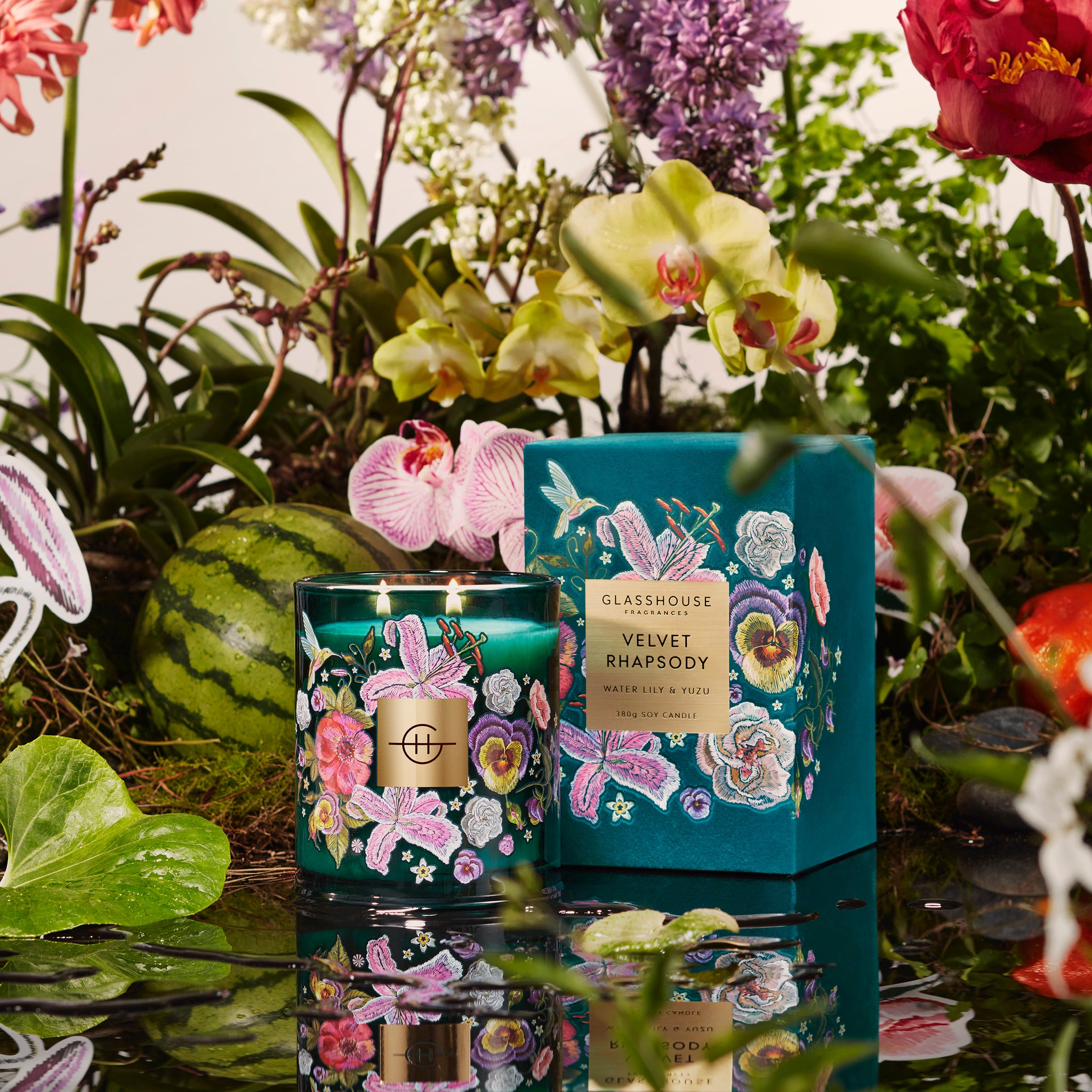 Glasshouse Fragrances Velvet Rhapsody Water Lily & Yuzu Soy Candle burning on a rainforest background