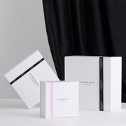 Glasshouse Fragrances Gift Box with black and pink ribbon on white tabletop with black curtain background