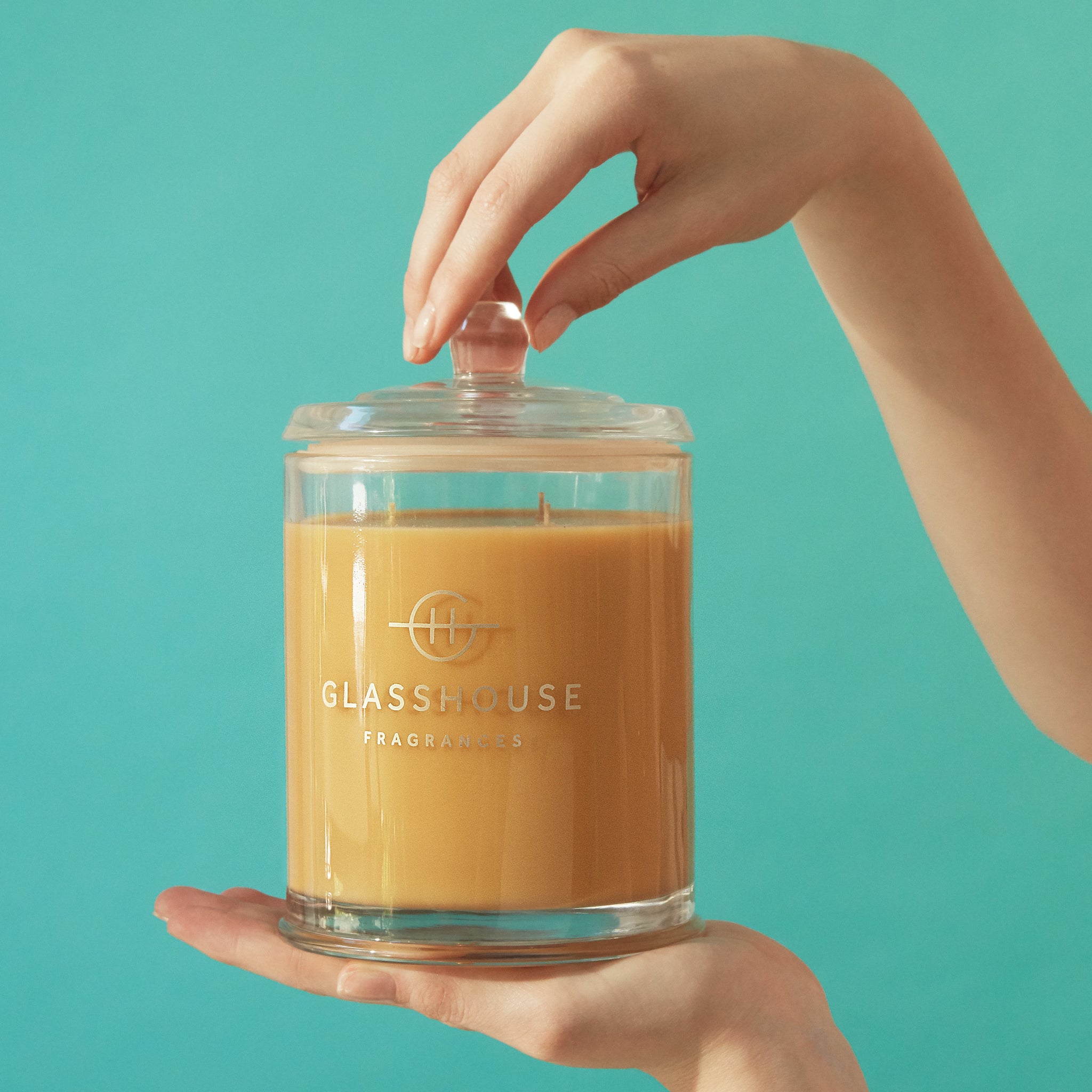 A Tahaa Affair 760g Vanilla Caramel Soy Candle held up by a pair of hands over a blue-green backdrop