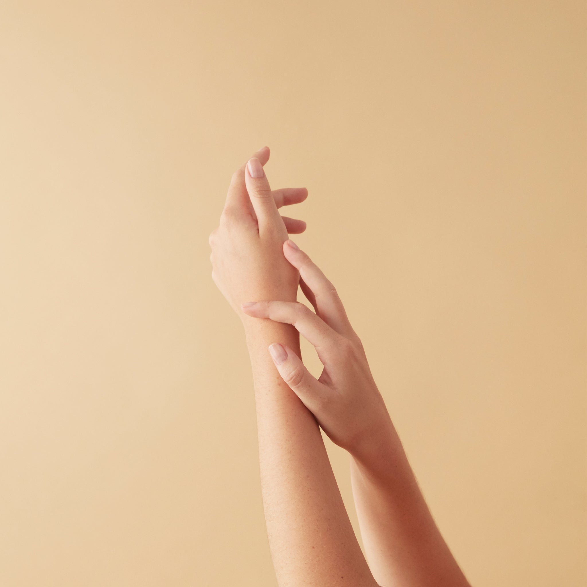Hands in air, one hand touching opposite wrist over yellow background