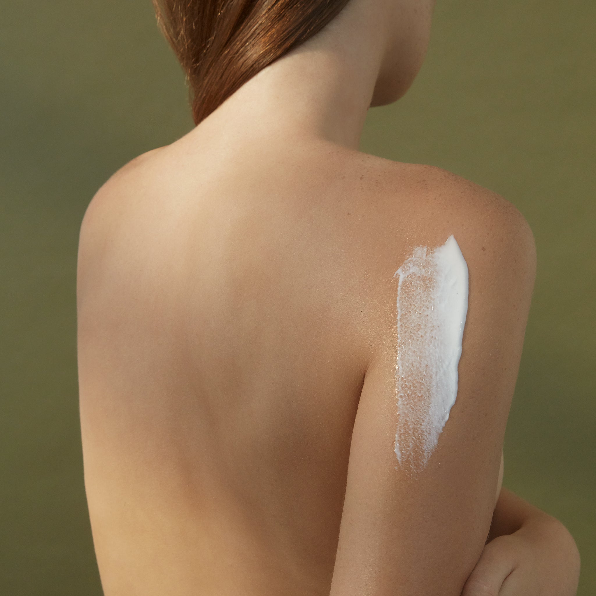 A woman's bare back with a smear of white cream on the back of her shoulder and arm